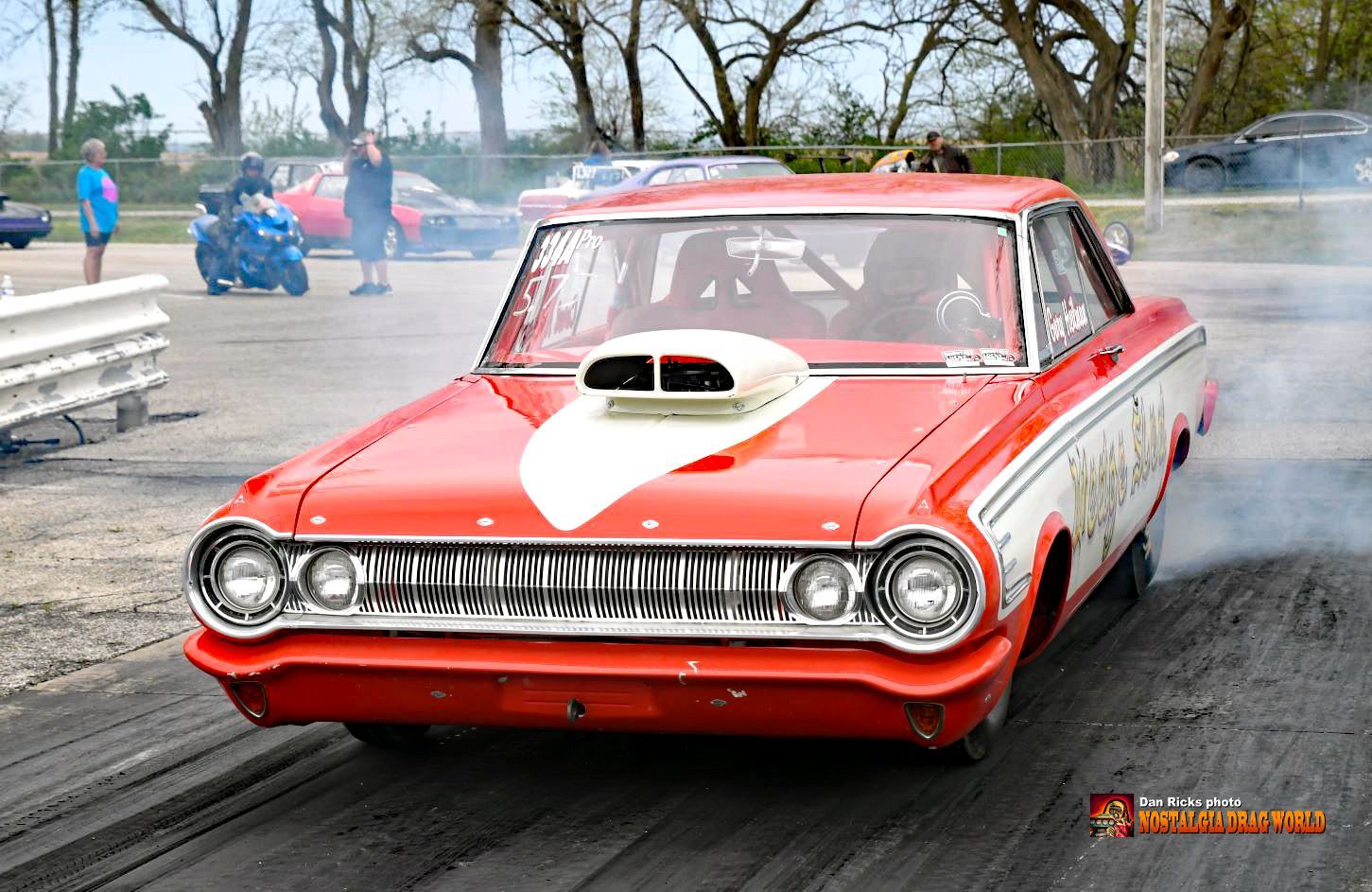 A red car with a hood scoop is doing a burnout