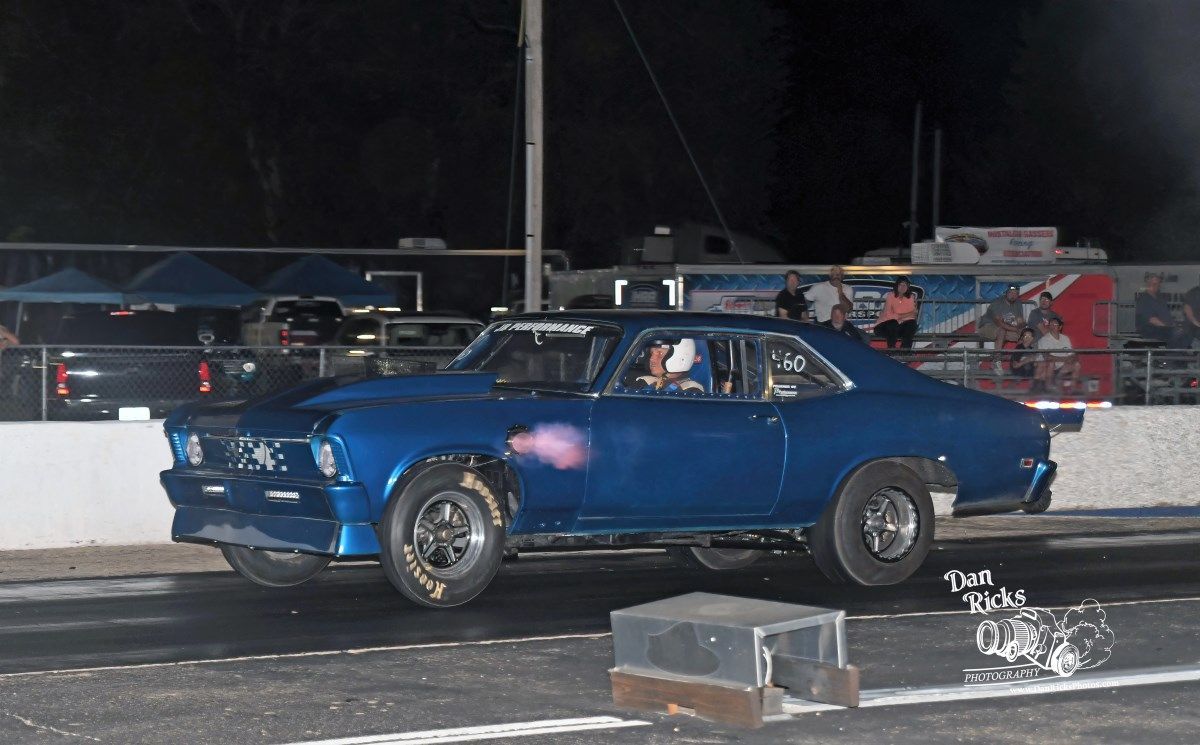 A blue car is driving down a race track at night