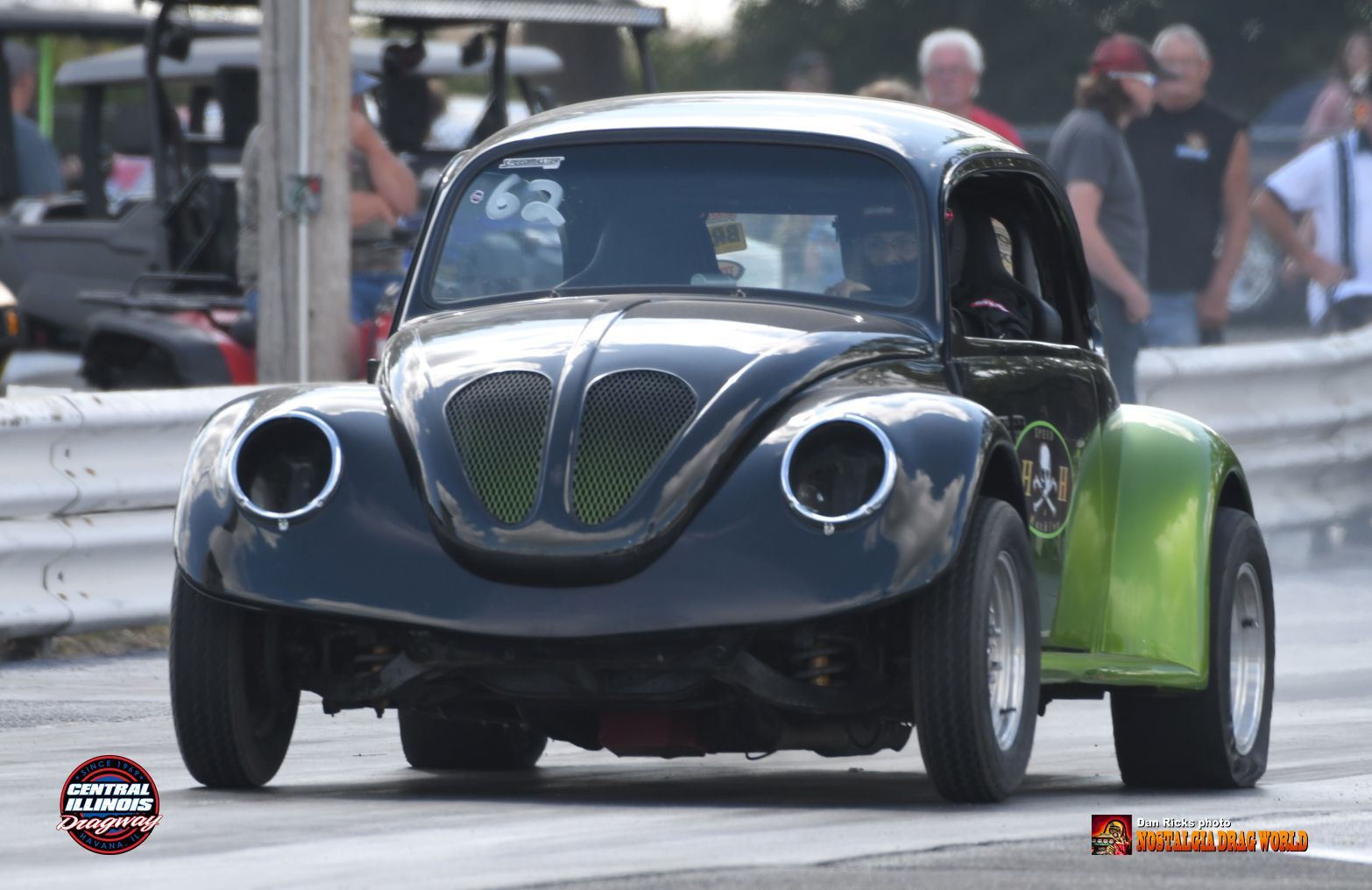 A black and green beetle is driving down a race track.