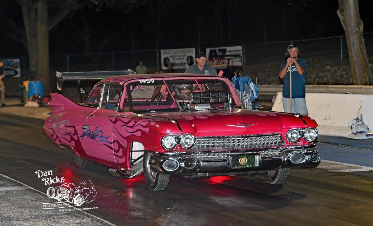 A pink car is driving down a race track at night.