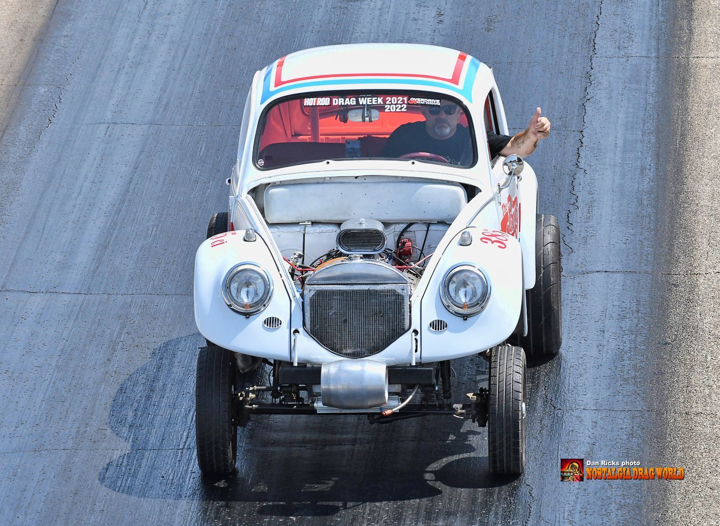 A white car with the hood open is driving down a road