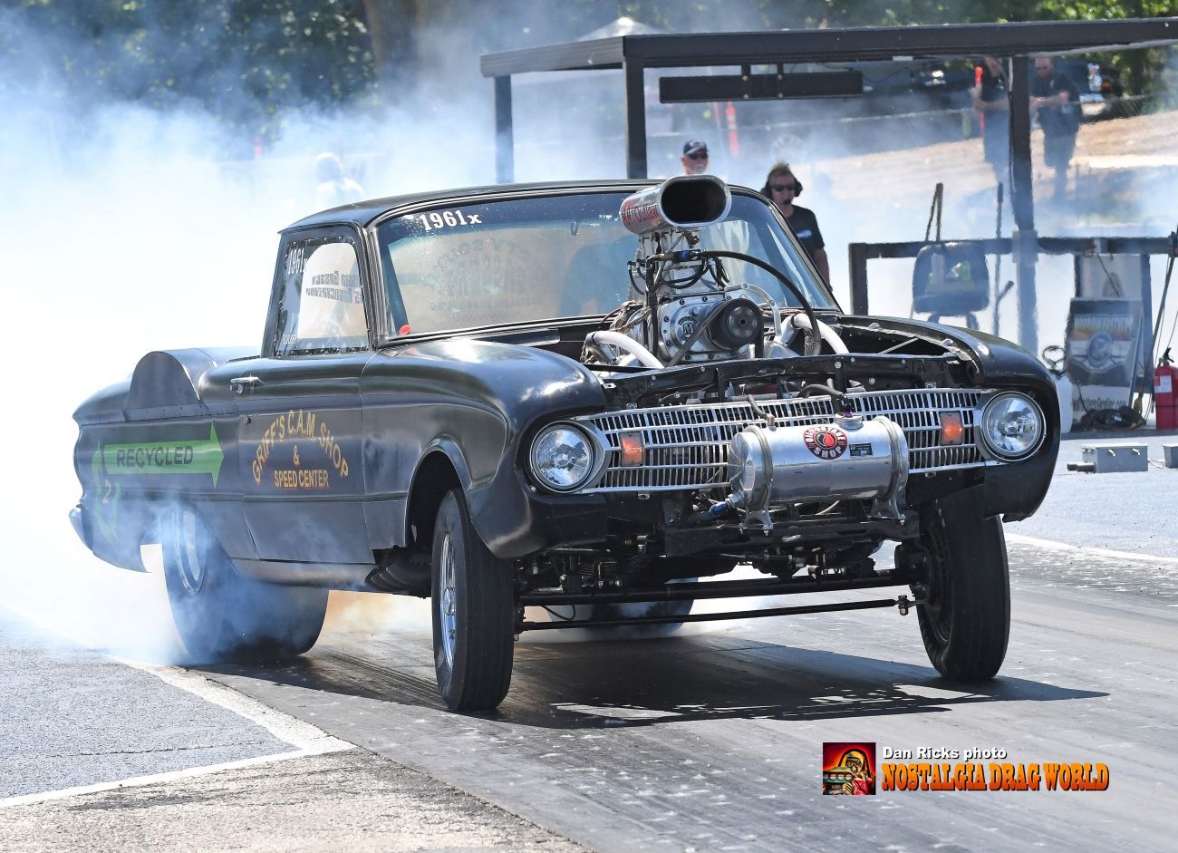 A car with smoke coming out of the hood is on a race track.