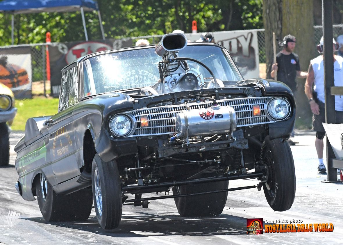 A black car with a huge exhaust pipe is driving down a race track.