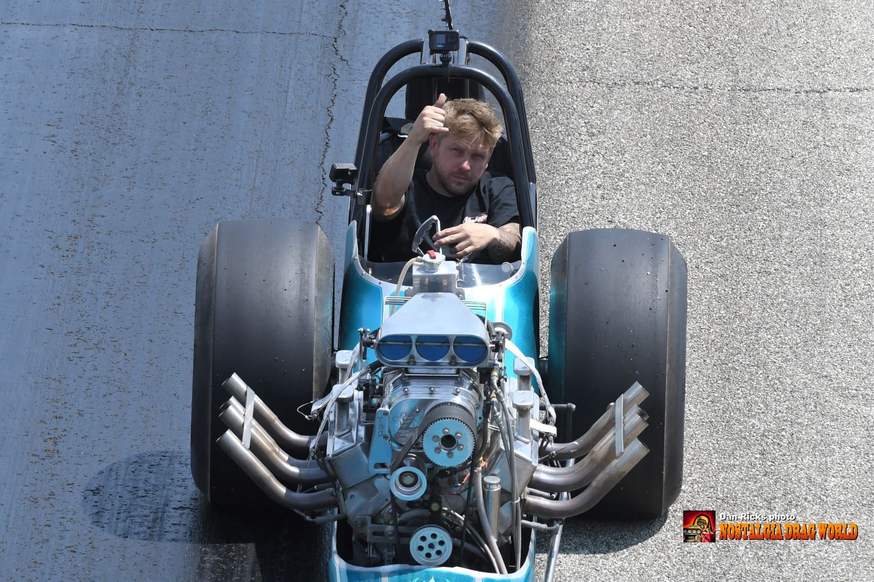 A man is sitting in a blue race car giving a thumbs up