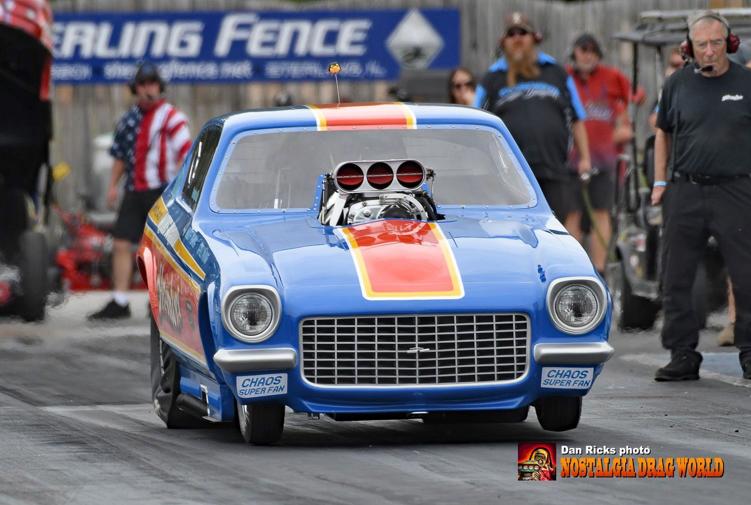 A blue race car is parked in front of a sign that says failing fence