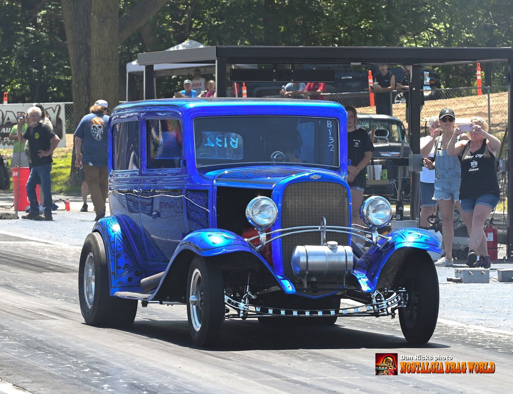 A blue car is driving down a road with people watching