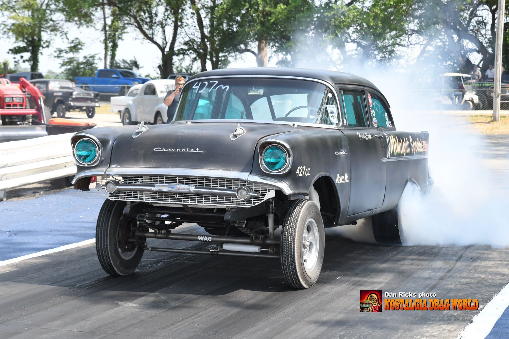 A black car is driving down a road with smoke coming out of the tires.