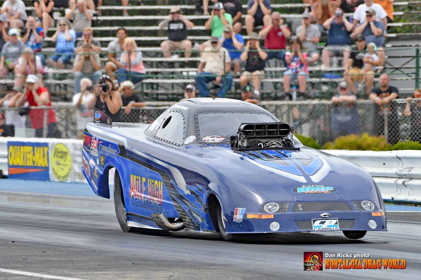 A blue race car is driving down a track in front of a crowd.