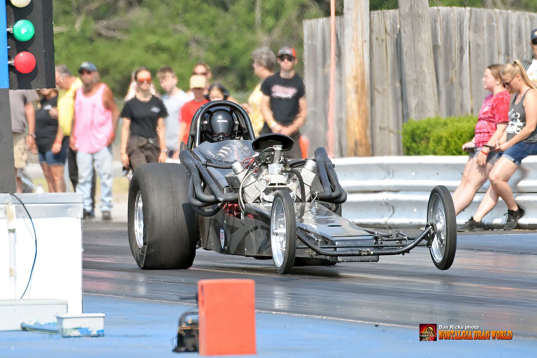 A dragster is driving down a race track with people watching.