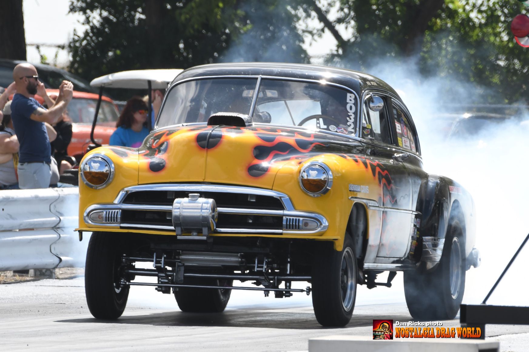 A yellow car with flames painted on it is doing a burnout on a race track.