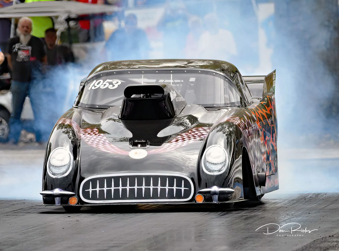 A black race car is doing a burnout on a race track.