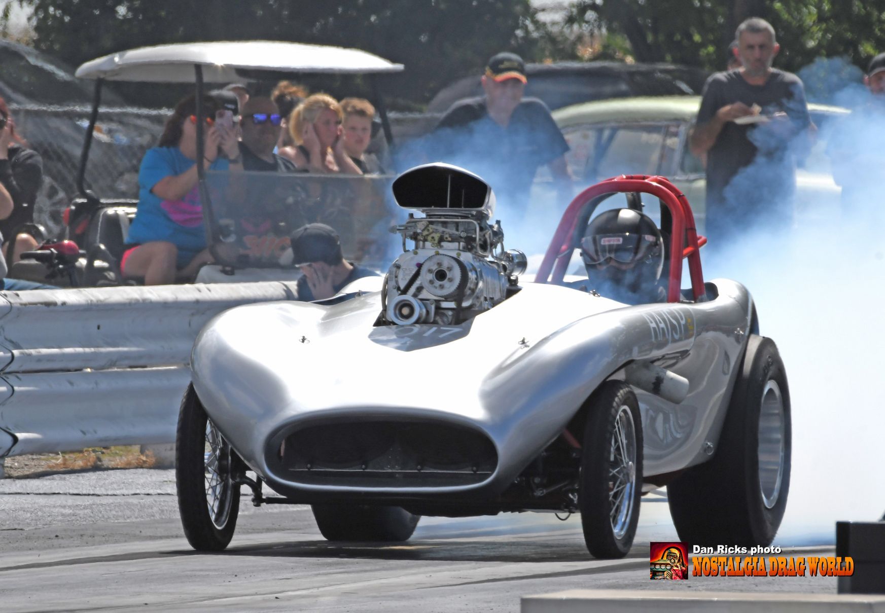 A silver race car with smoke coming out of the engine