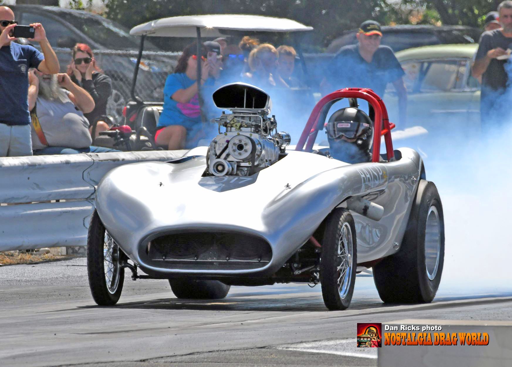 A silver race car with a large engine is driving down a track