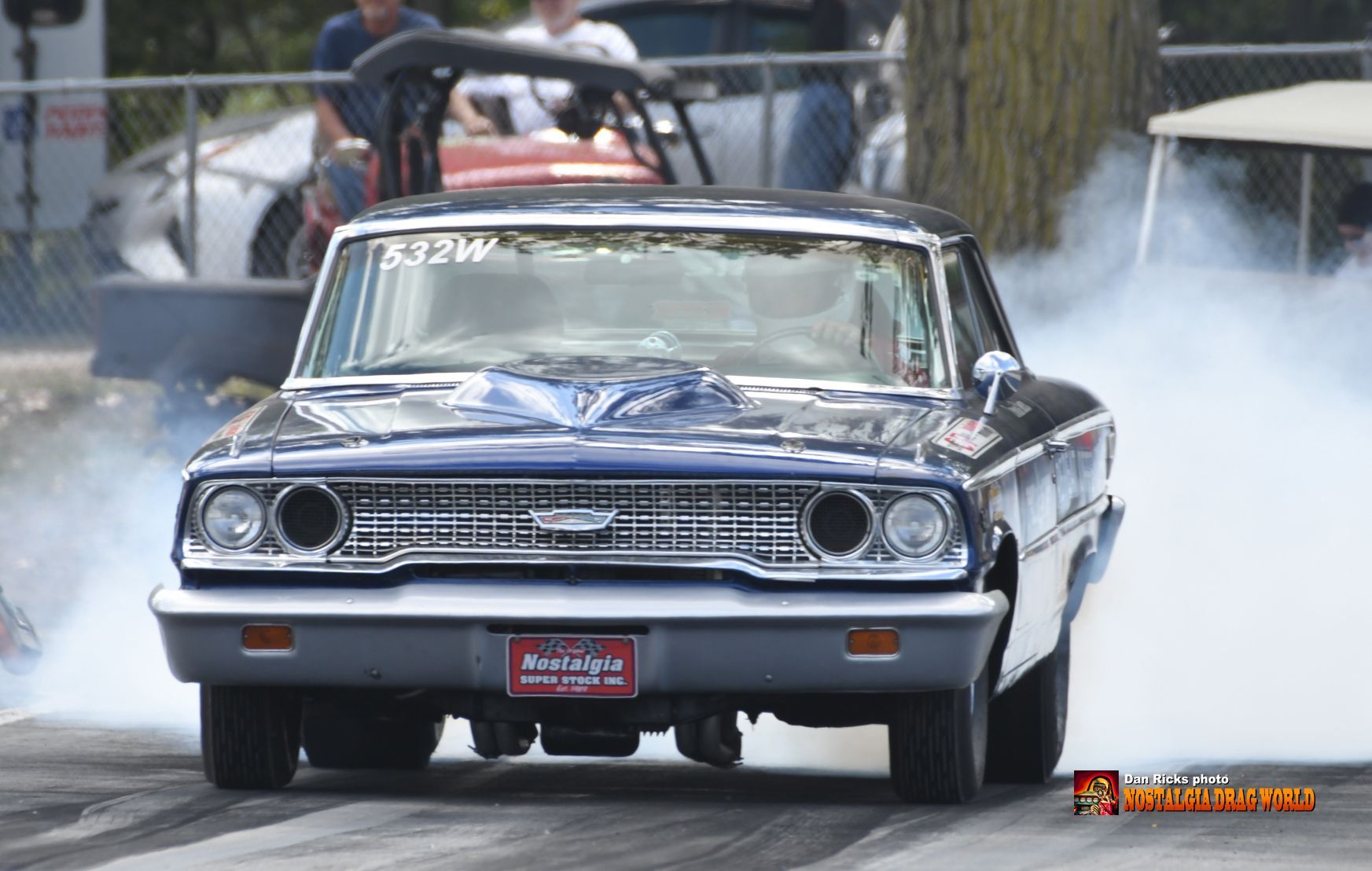 A blue and white car is doing a burnout on a race track.