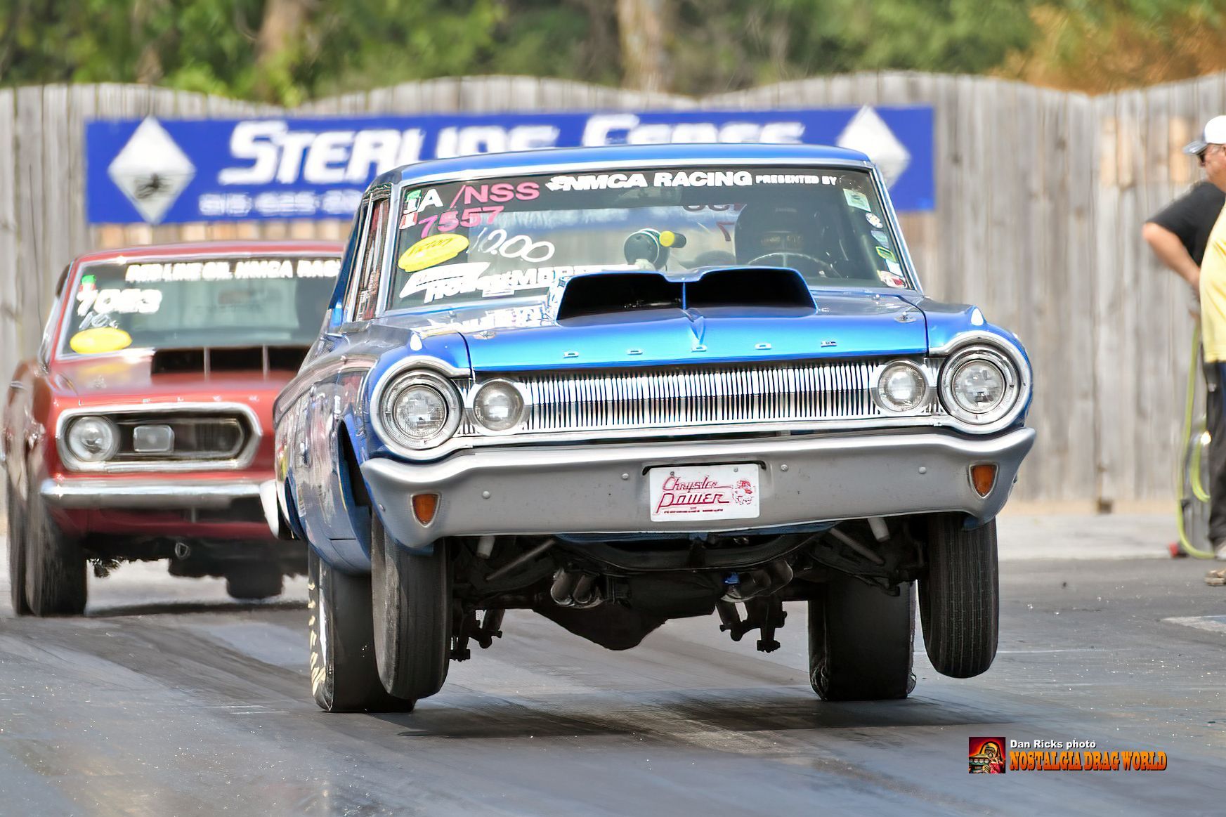 A blue car is driving down a race track next to a red car