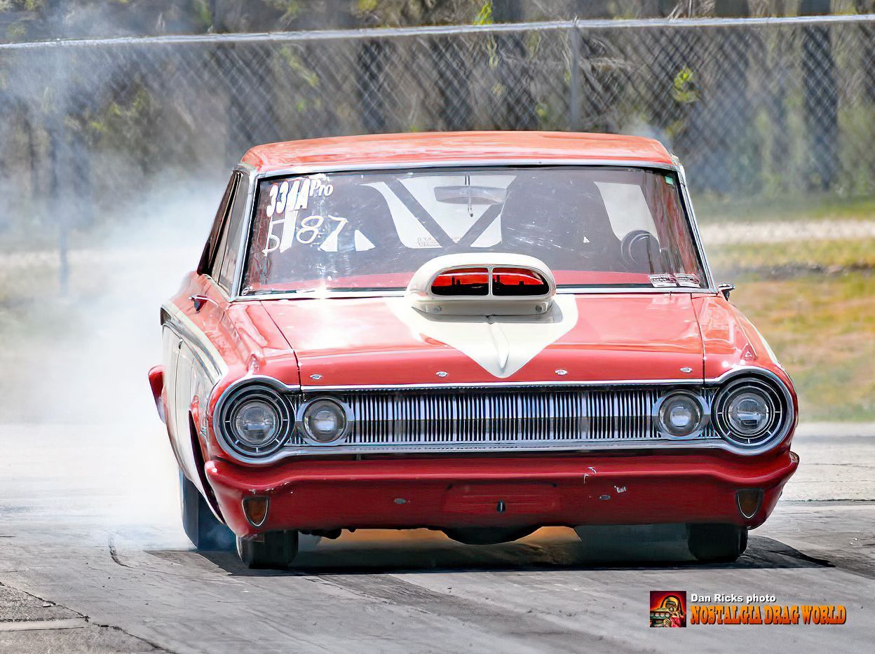 A red car with the number 87 on the windshield is driving down a track.