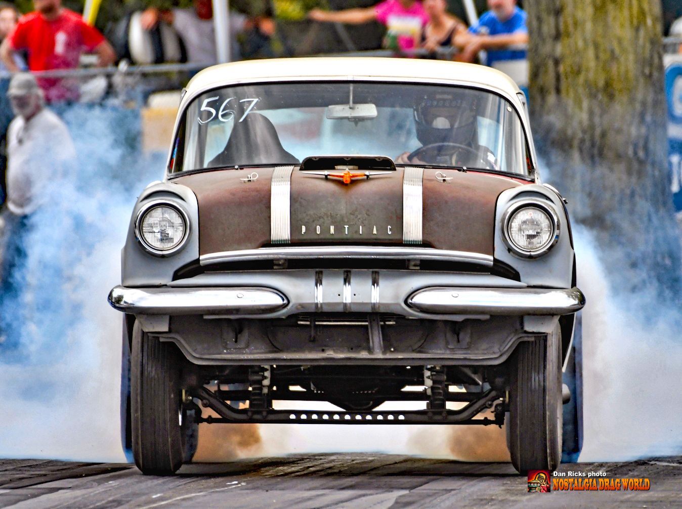 A car with the number 567 on the windshield is doing a burnout