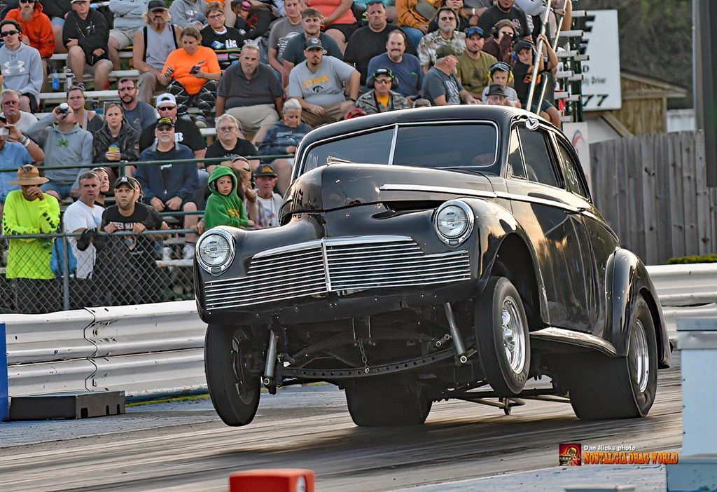 A black car is driving down a race track in front of a crowd.