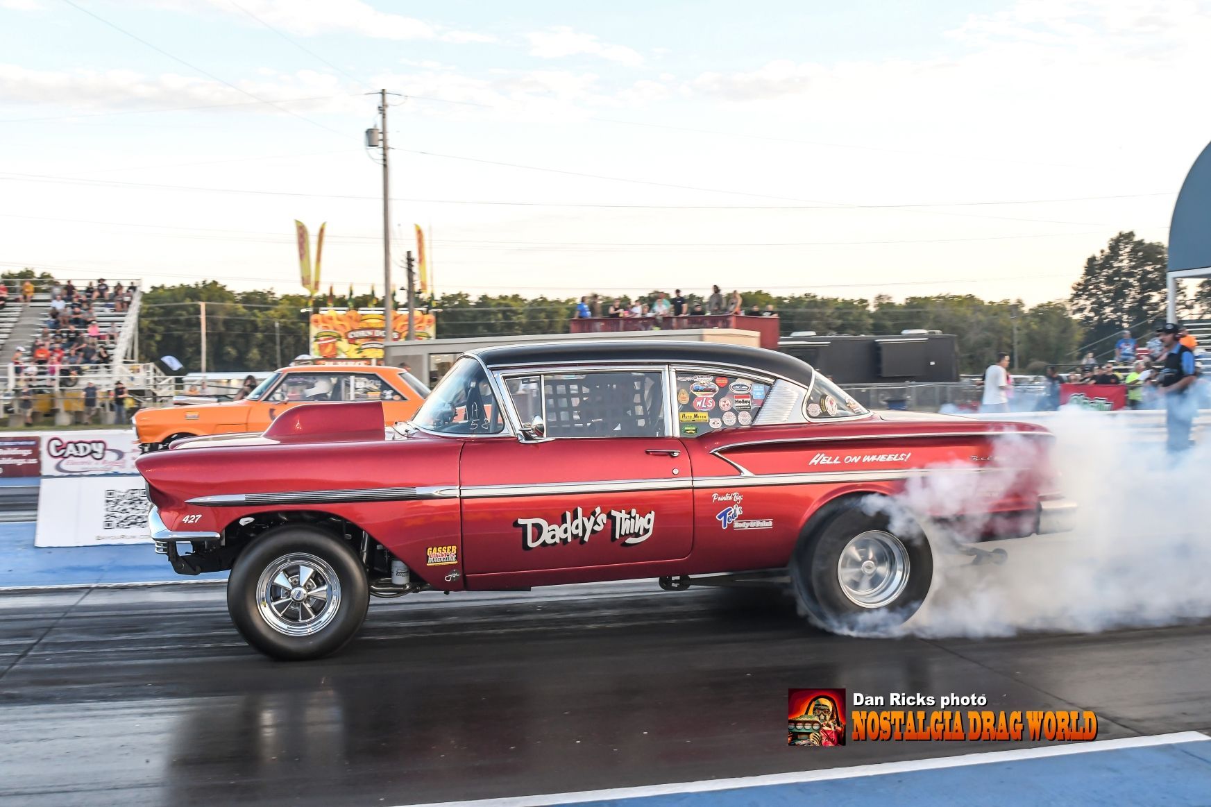 A red car is doing a burnout on a race track.