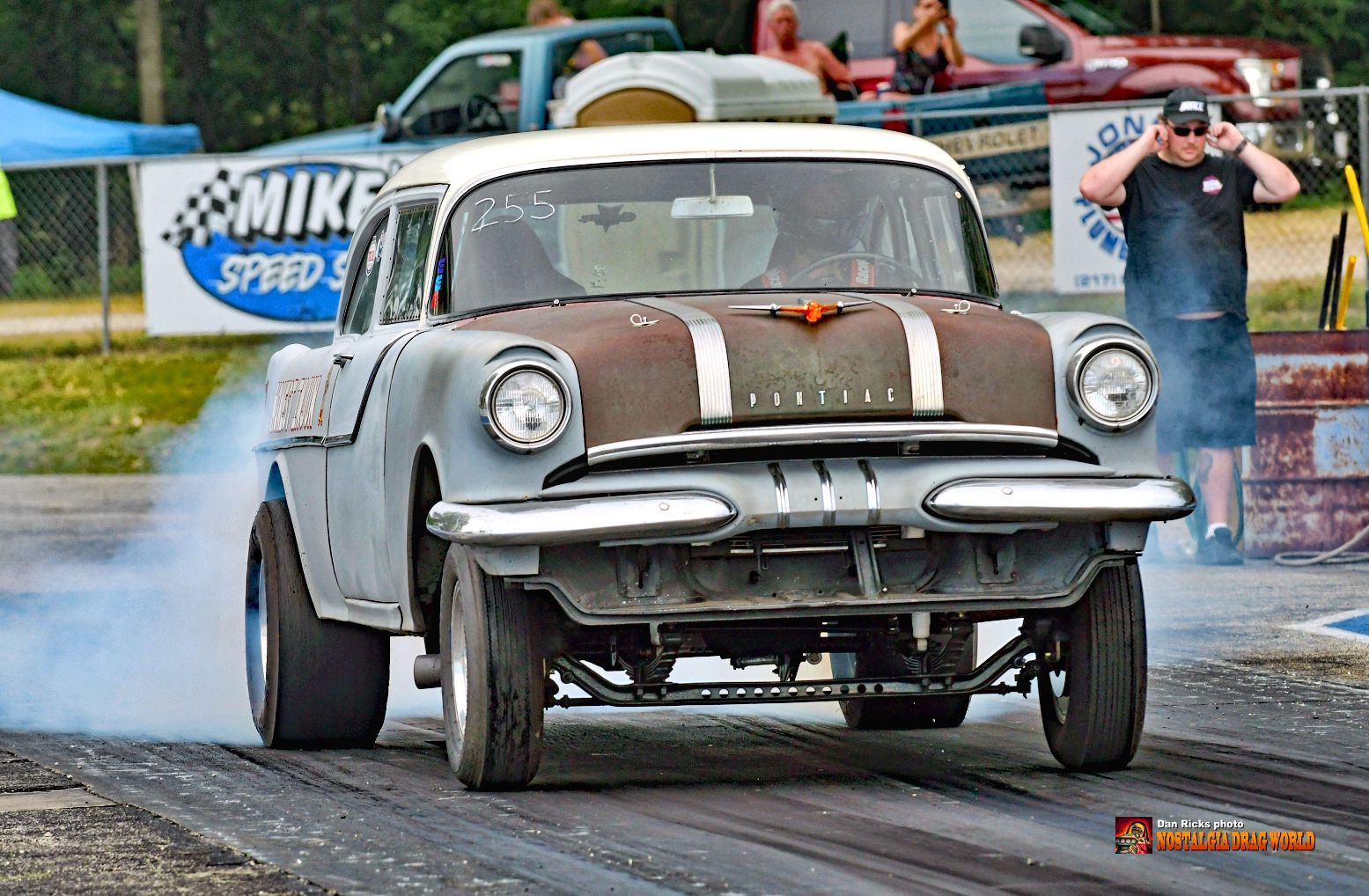 An old car is doing a burnout on a race track.