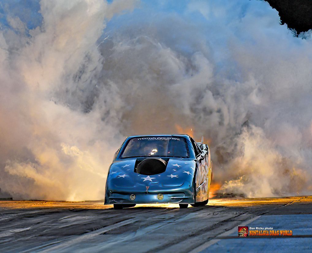 A blue race car is driving down a track with smoke coming out of the hood.