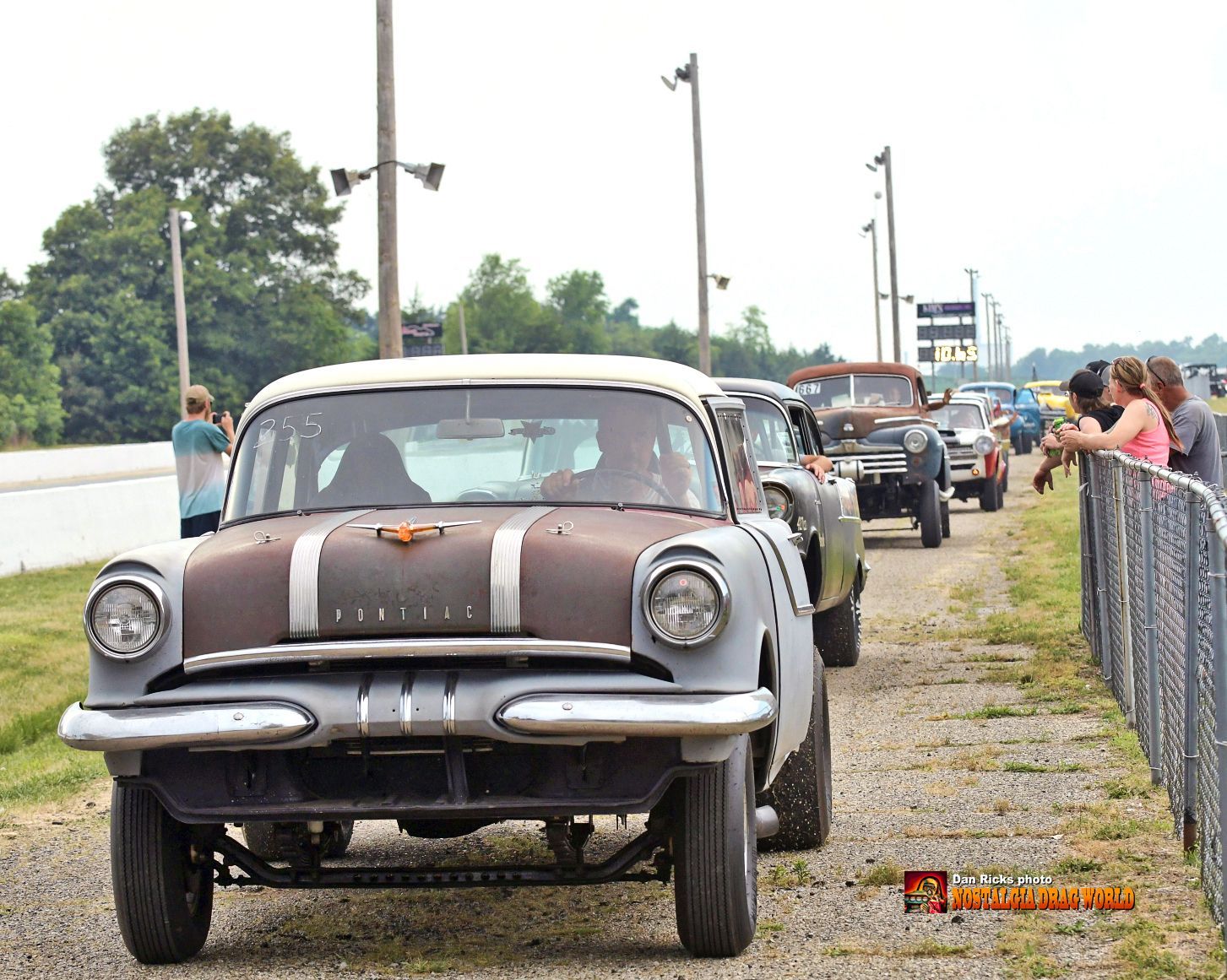 A row of old cars are parked on a gravel road
