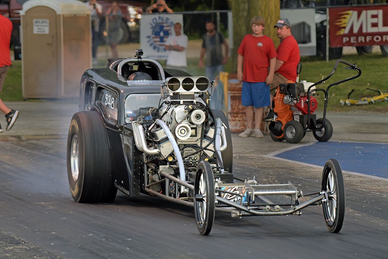 A dragster is driving down a race track with people watching.