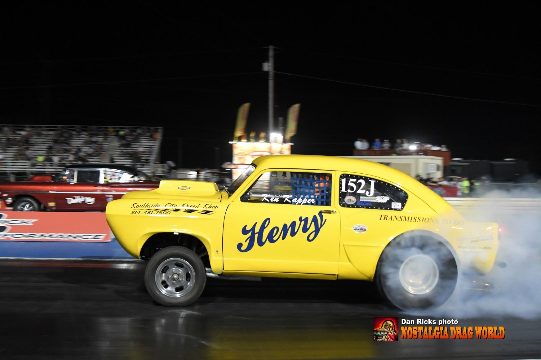 A yellow car with the name henry on the side is on a race track.