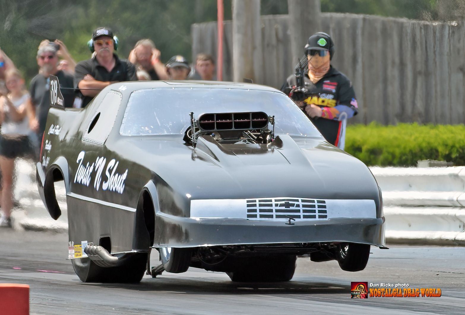 A black race car is driving down a track with people watching.