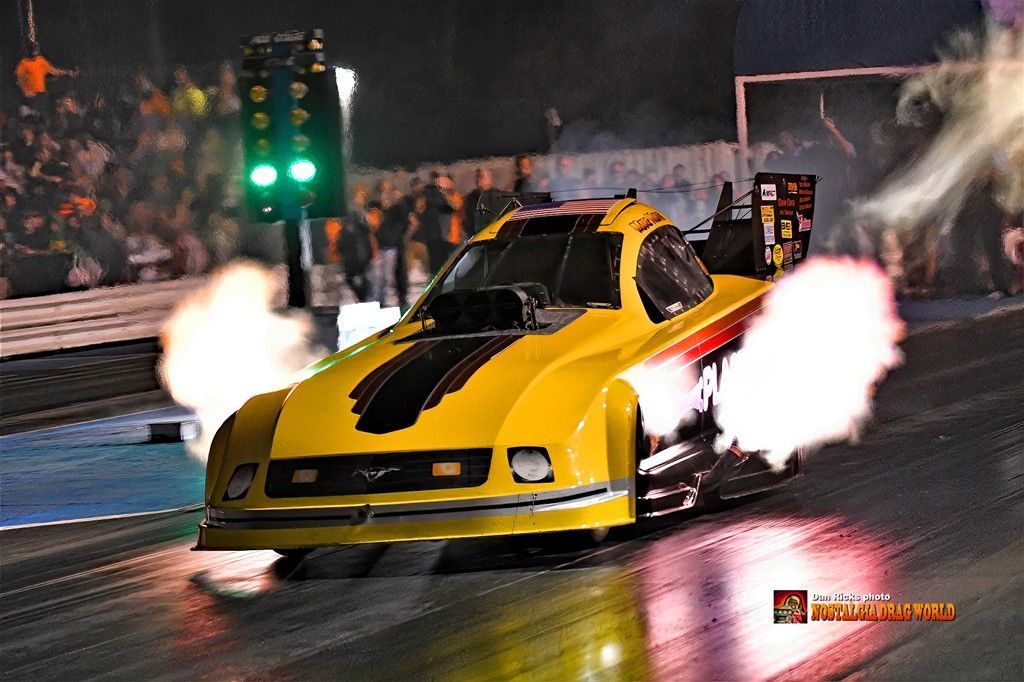 A yellow race car is driving down a track at night