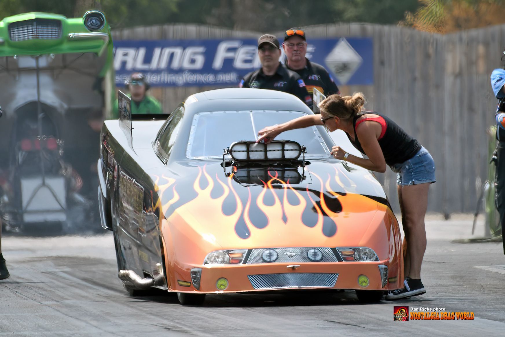 A woman is standing next to a race car with flames on it.