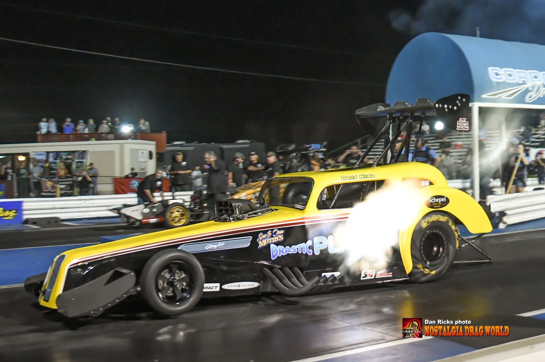 A yellow race car with a flame coming out of the exhaust pipe