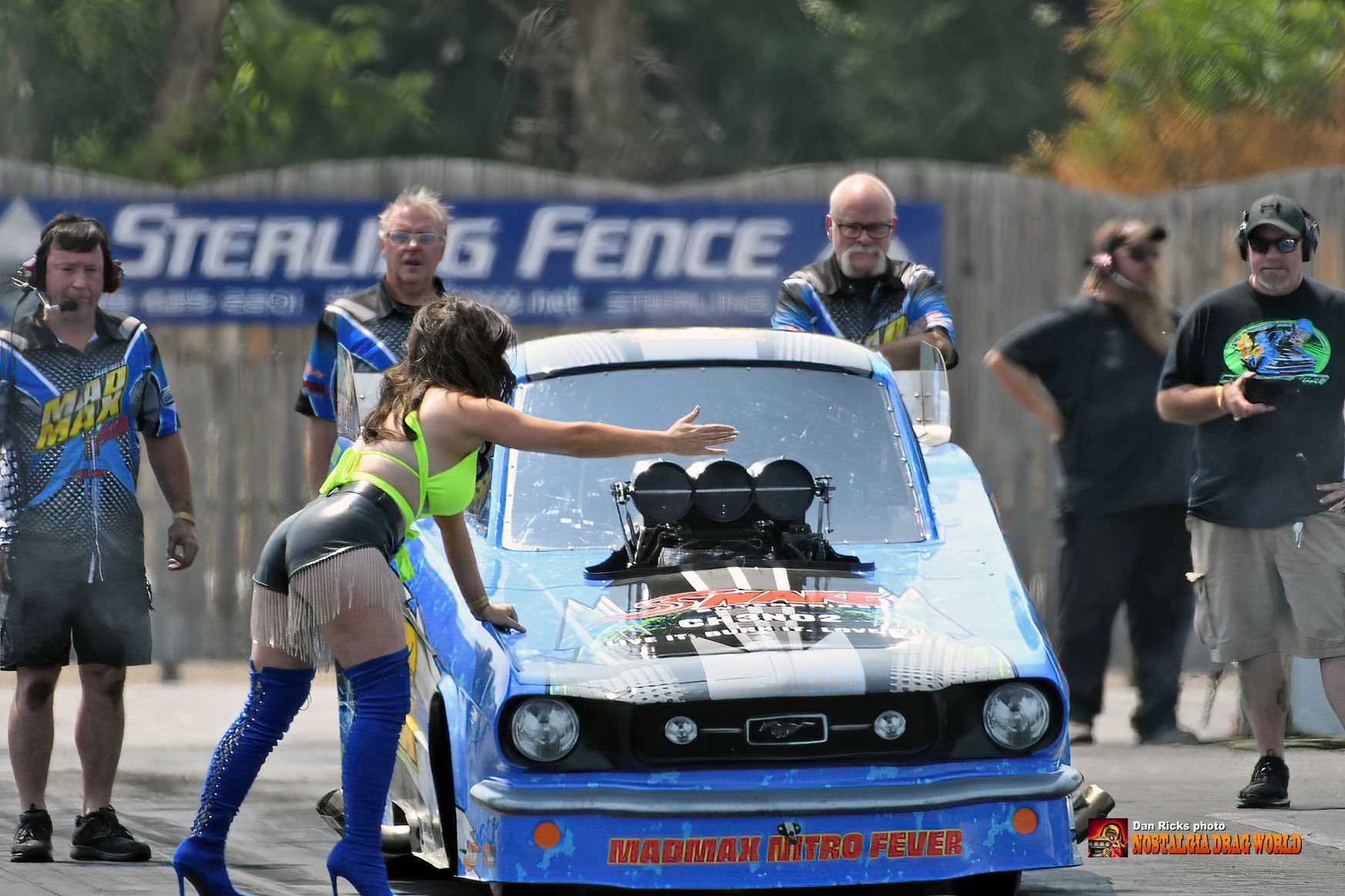 A woman is pushing a drag race car on a track.