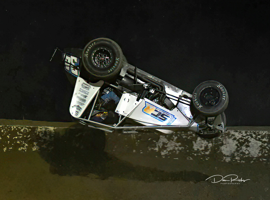 A race car is upside down on the side of the road