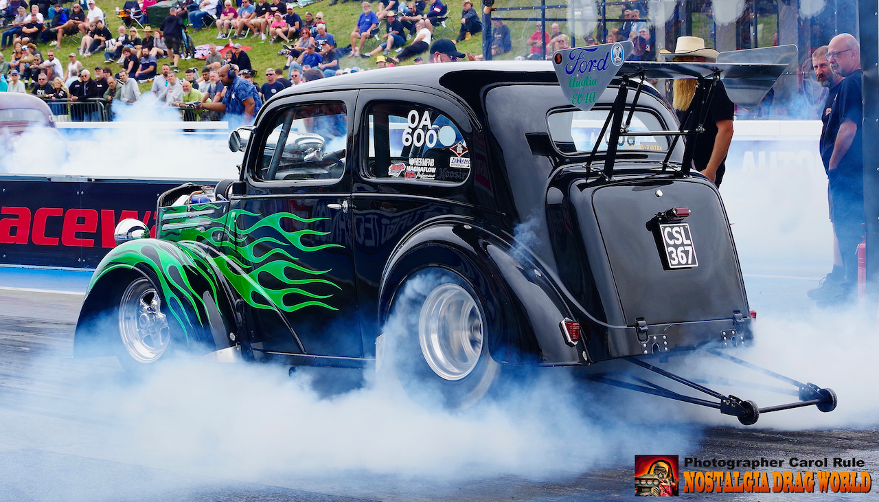 A black car with green flames painted on it is doing a burnout on a race track.