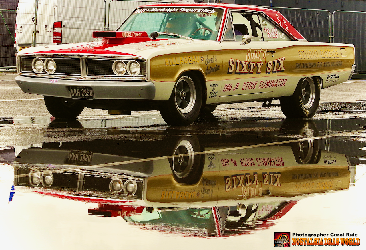 A sixty six muscle car is reflected in a puddle of water