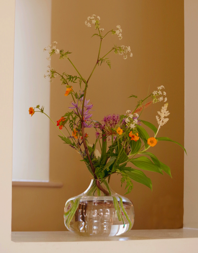 A vase filled with flowers is on a shelf in front of a window.
