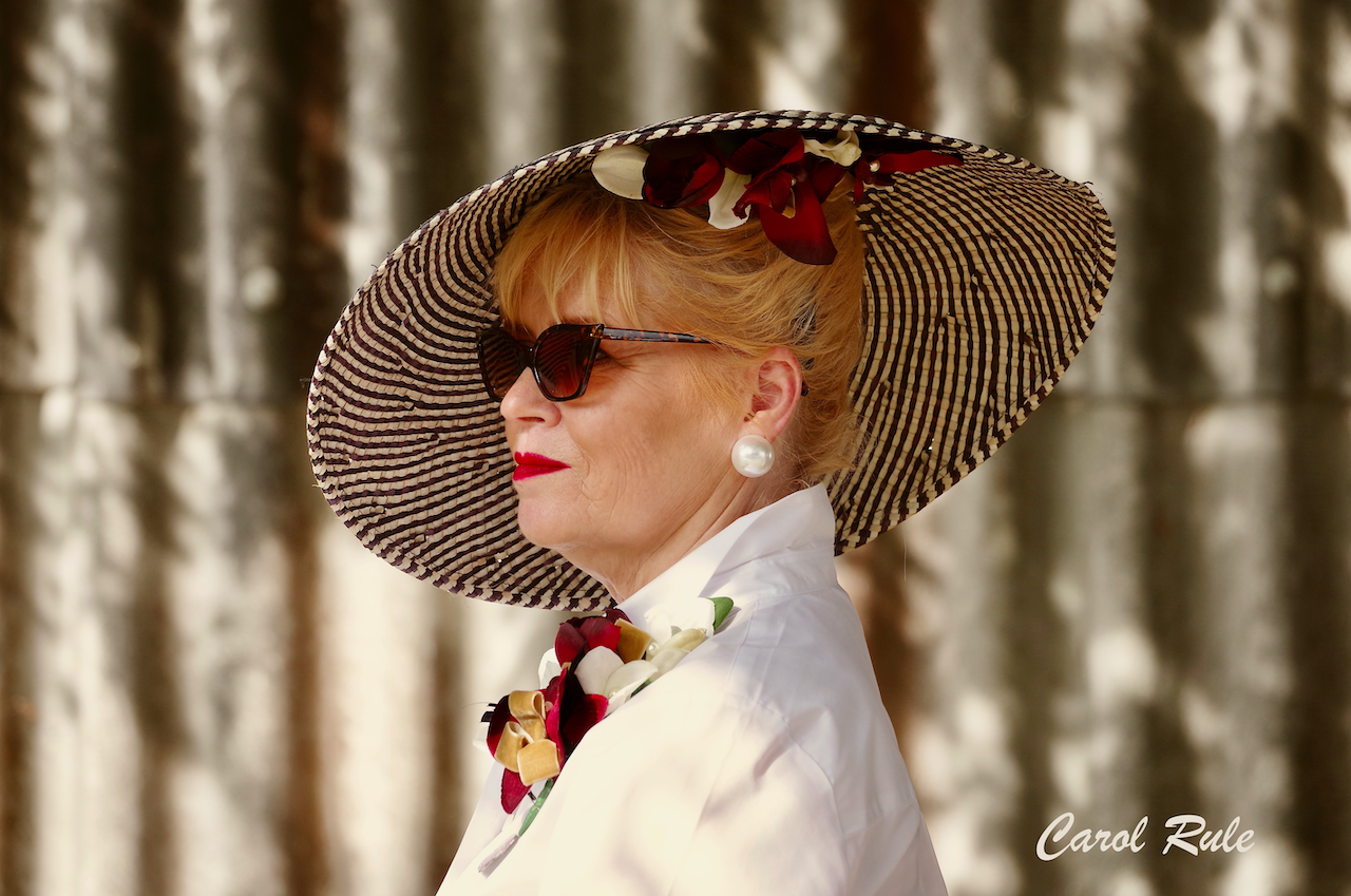 A woman wearing a hat and sunglasses is standing in front of a wall.