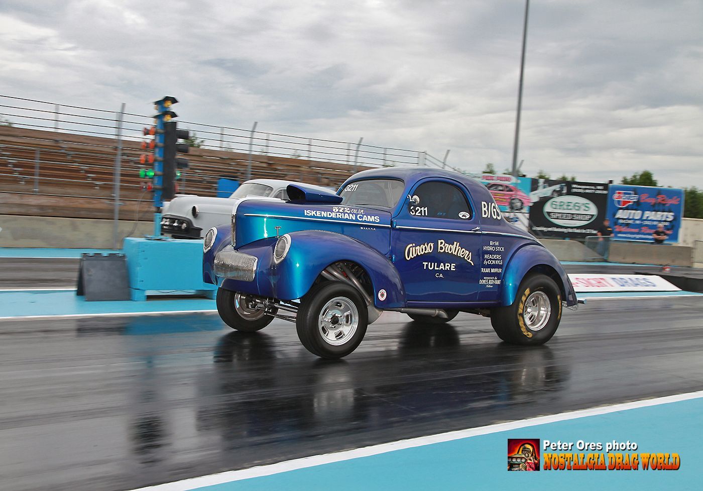 A blue car is driving down a wet race track