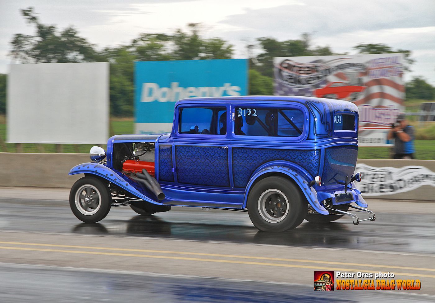 A blue car is driving down the road in front of a doheny 's sign