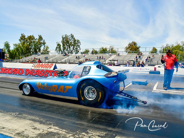 A blue dragster is driving down a race track