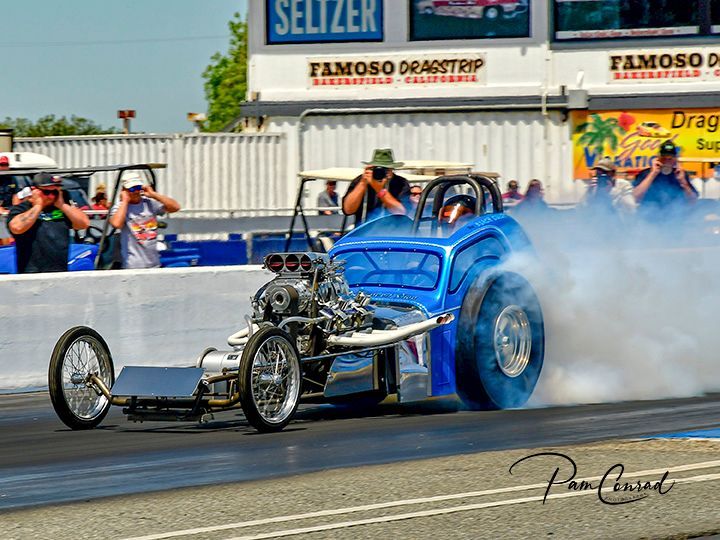 A blue dragster is driving down a track with smoke coming out of the tires.