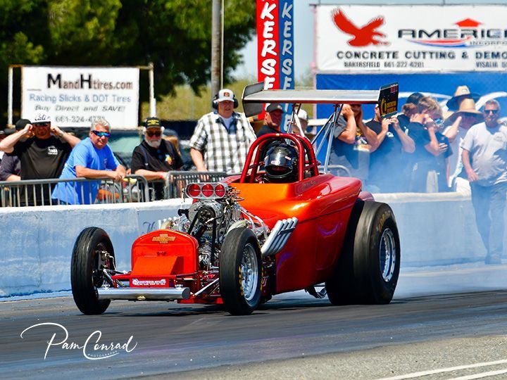 A red race car is driving down a track in front of a crowd