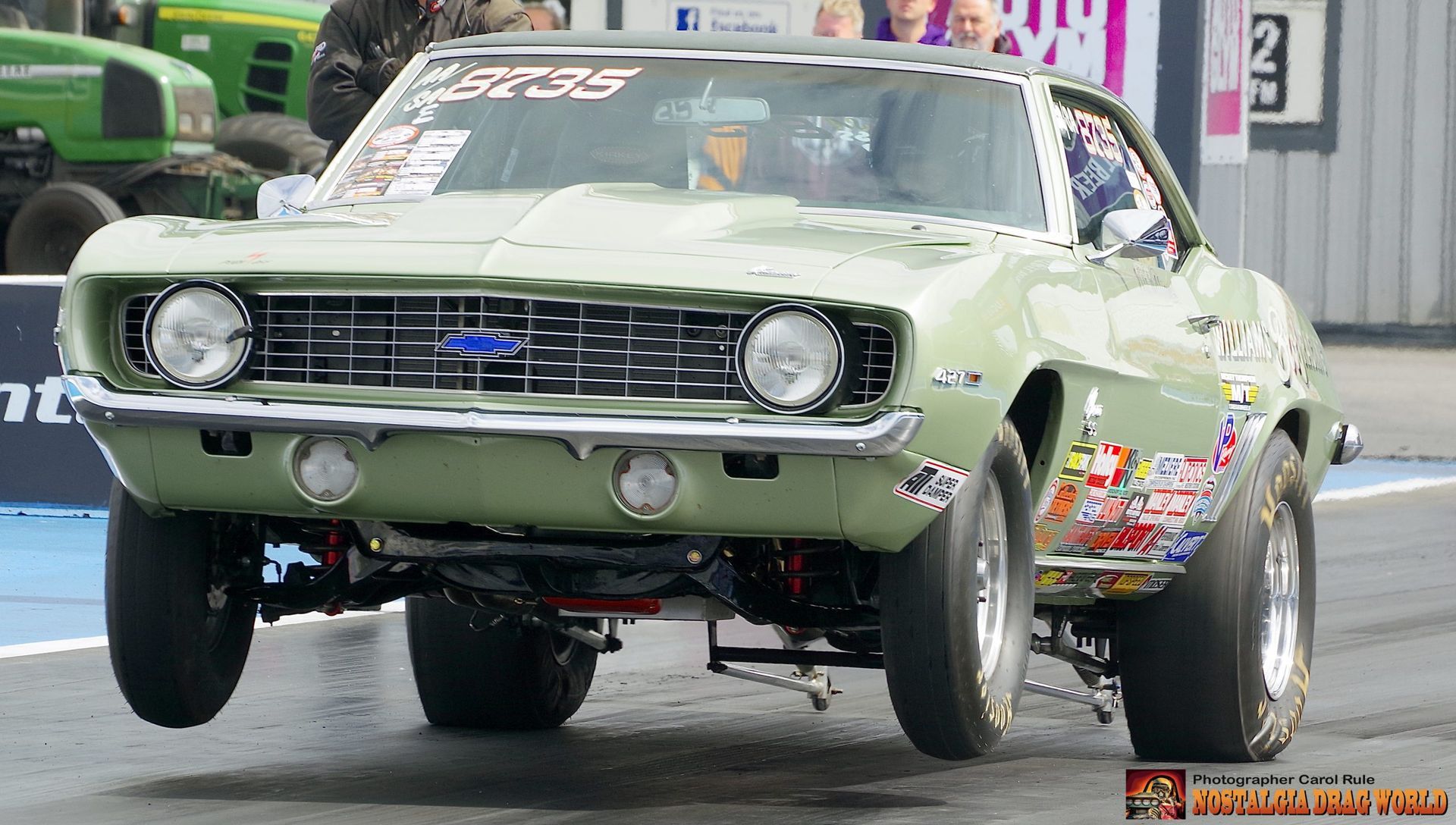 A green muscle car is parked on a race track.