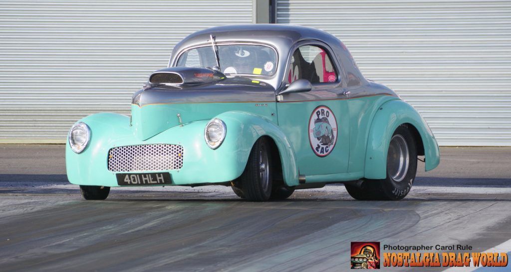 A green and silver car is driving down a race track.