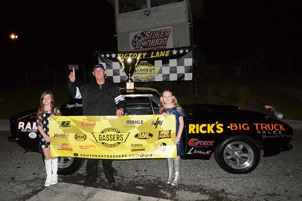 A man is holding a trophy in front of a car that says rick 's big truck.
