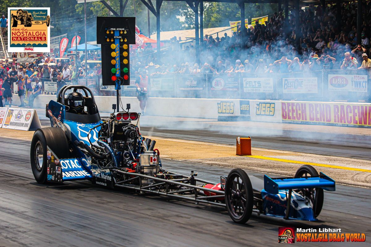 A blue dragster is driving down a race track.