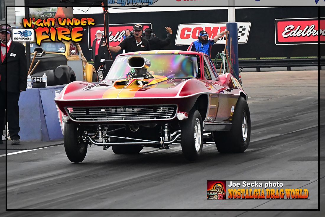 A red car is on a race track with a sign that says night under fire