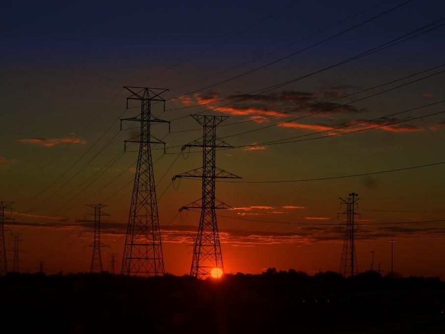 The sun is setting behind a row of power lines.