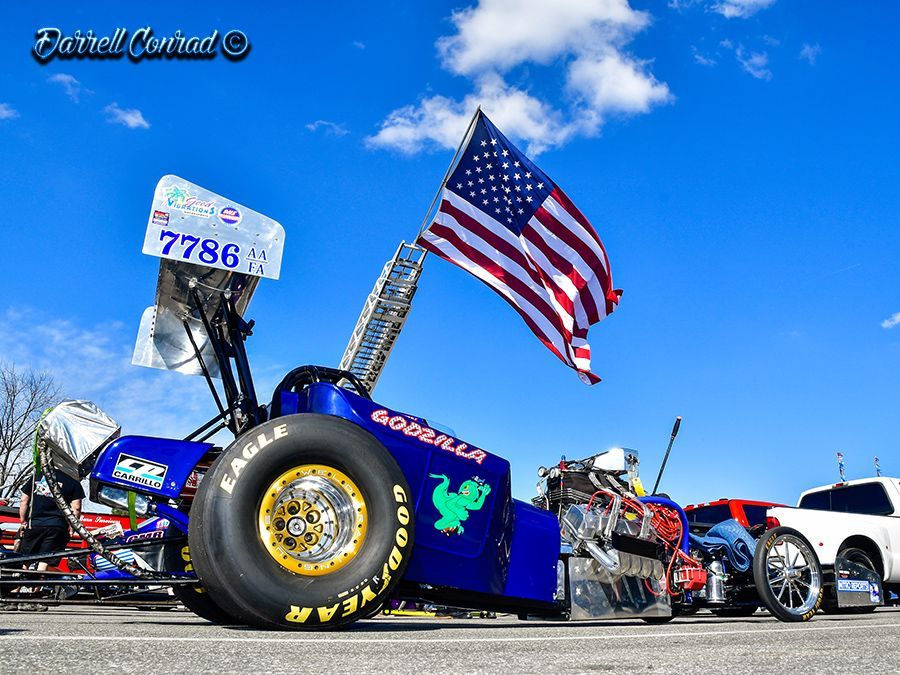 A blue racing car with an american flag on the back is parked in a parking lot.